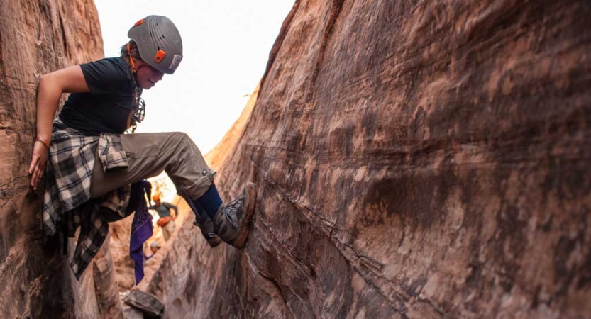 A person braces themselves on opposite walls of a slot canyon